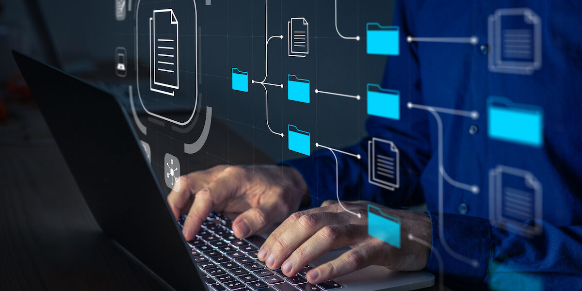 Document Management System (DMS) being setup by IT consultant working on laptop computer in office. Software for archiving, searching and managing corporate files and information. Business processes computer laptop and typing