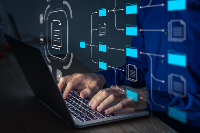 Document Management System (DMS) being setup by IT consultant working on laptop computer in office. Software for archiving, searching and managing corporate files and information. Business processes computer laptop and typing